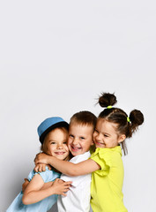 Studio portrait of children on a light background: full body shot of three children in bright clothes, two girls and one boy. Triplets, brother and sisters. hugging on camera. Family ties, friendship