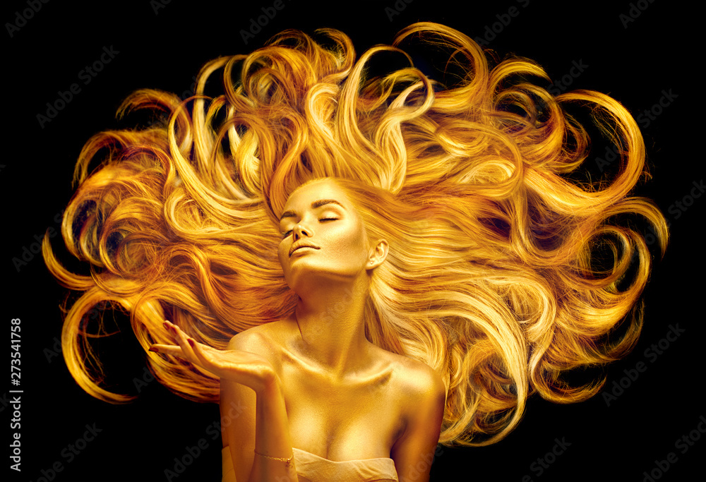 Golden beauty woman. Sexy model girl with golden makeup and long hair pointing hand over black. Metallic gold glowing skin and fluttering hair - obrazy, fototapety, plakaty 