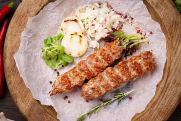 Traditional Adana kebab on wooden plate with marinated onion garnishing and spicy aromatic herbs. Delicious meat, Turkish cuisine