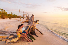 Beach Sunset Couple Relaxing On Summer Honeymoon Vacation Travel Watching Sunset At Florida Beach, Gulf Of Mexico, USA Travel. Man And Woman At Lover's Key.