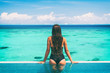 © Maridav - Sexy swimsuit model at luxury infinity pool overwater bungalow hotel showing off cheeky black lace fashion one piece. Turquoise ocean sea woman from behind.