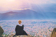 © raisondtre - Young woman sitting on top of cliff in summer mountains at sunset and enjoying beautiful view of nature landscape cityscape. Monastery Meteora Kalambaka town in Greece Europe. Wanderlust adventure.