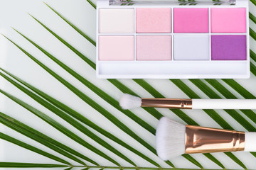 On the green branch is a palette of pink eye shadows and makeup brushes.