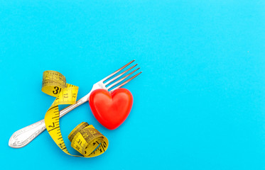 Fork with measuring tape and red heart on blue. top view. Space for text. Healthy lifestyle concept.