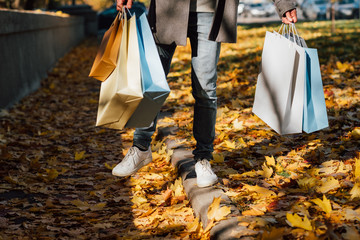 Wall Mural - Autumn fun. Cropped shot of man walking with shopping bags, enjoying fall season with yellow leaves covering sidewalk.