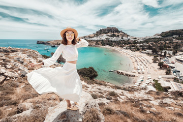 Wall Mural - Happy asian woman travels in Greece. Having fun at the stunning view on sea resort and old town of Lindos on the mountain