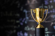 Achievement success in education awards concept: Golden trophy cup winner on blur formula equation blackboard background. Congratulation in university.