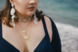 Attractive busty curvy woman in a blue swimsuit on the beach. Stylish accessories, fringe, fashion for plus size, beautuful sea. Bodypositive, natural authentic beauty, resort, summer vacation. Copy