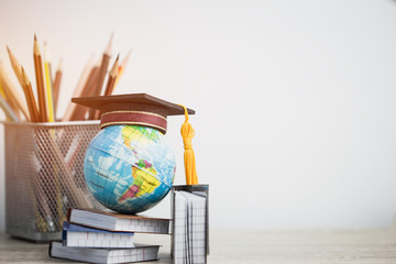 Concept of global business study abroad education. Graduation hat on models globe, books with pencils on wood white background. Congratulations to graduated, Studies lead to success. Back to School