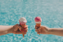 Two Friends Hold Pink Ice Cream On A Hot Day On Background Of A Blue Pool. Hands With A Beautiful Manicure, The Concept Of Leisure, Summer Vacation. Copy Space.