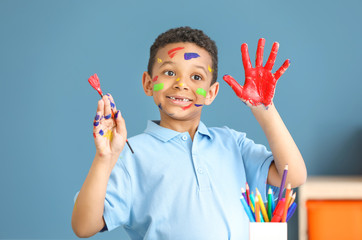 Cute African-American boy with hands and face in paint at home