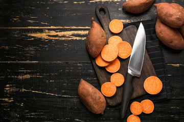 Cutting board and knife with raw sweet potato on wooden background