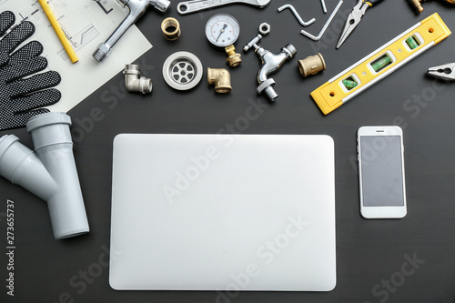 Fotografía Modern laptop, mobile phone and plumbing items on dark background