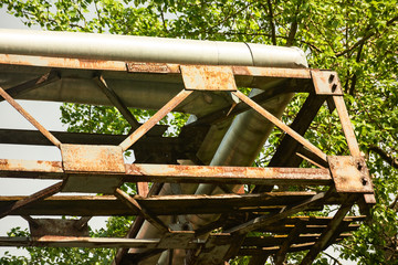 Rusty metal construction with industrial heating pipes against a green tree