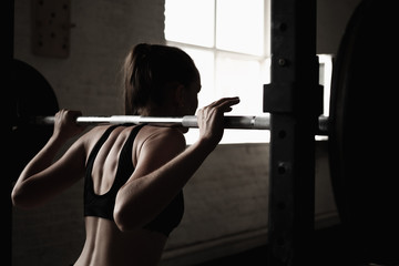 Fit young girl doing squats with barbell. Cross training workout. The sporty back of a girl..