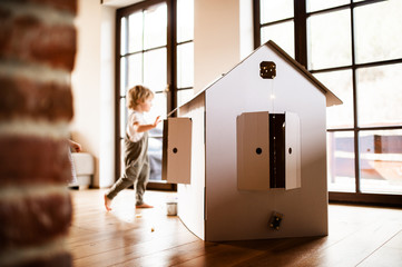 A toddler boy playing with a carton paper house indoors at home.