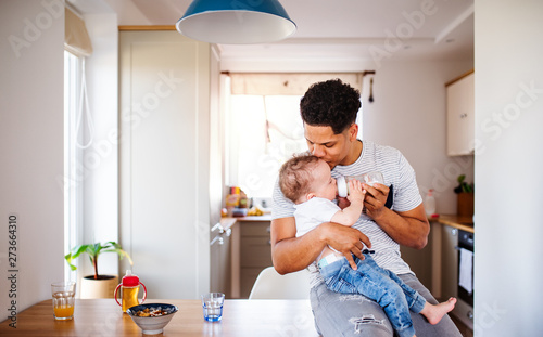 A father bottle feeding a small toddler son indoors at home. Wallpaper Mural