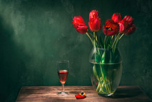 Classic Still Life With Beautiful Red Tulip Flowers Bouquet In Transparent Glass Vase And A Glass Of Red Wine. Art Photography.