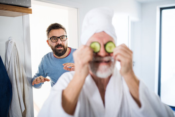 Wall Mural - An adult hipster son and senior father in bathroom indoors at home, having fun.