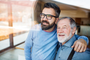 Wall Mural - Adult son and senior father indoors at home, looking out. Shot through glass.