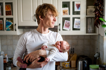 Wall Mural - Young father holding a newborn baby in kitchen at home.