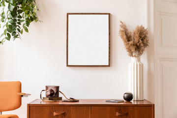 Stylish room of home interior with brown mock up frame with vintage accessories, retro camera, orange chair and flowers in vase. Cozy home decor. Minimalistic concept. Retro composition of cupboard.