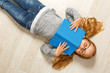 © Olga - Cute little girl in glasses with a book lying on the floor