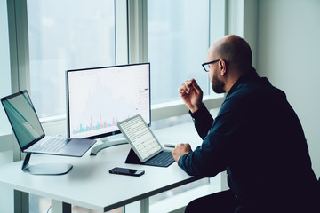 Young man employee working on PC and laptop computers with financial information graphs on screen sitting at office table. Successful businessman accounting revenue and making research.Millennial work