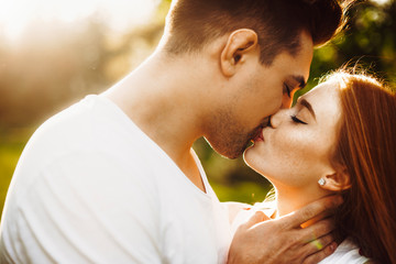 Wall Mural - Close up portrait of a amazing caucasian female with freckles and red hair kissing with her boyfriend outside against sunset while traveling.