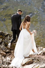 Wall Mural - Unrecognizable bride walking in the mountains with a bucket in one hand and holding with another hand her groom .