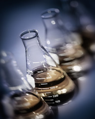 Selective focus background image showing row of chemical flasks with gold liquid on blue grey