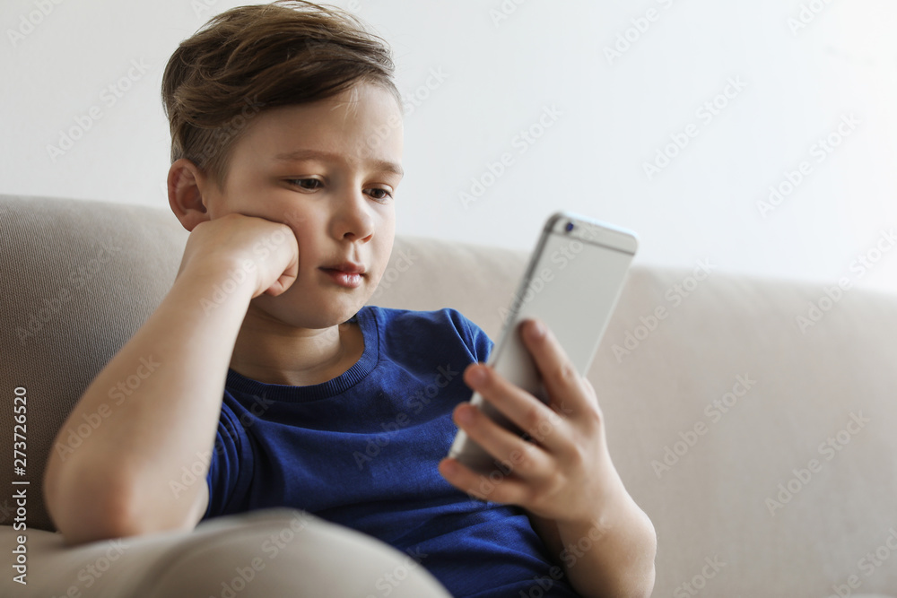 Little child with smartphone on sofa in room. Danger of internet