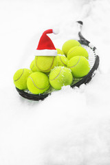 Wall Mural - Tennis winter concept with tennis balls and racket on white snow, isolated. Top view, copy space. Merry Christmas and Happy New Year sport healthy layout. Santa Claus hat on the top off ball.