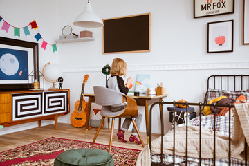 Genderless bedroom with kid painting at the retro desk in tenement house