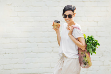 Wall Mural - Young woman in light summer clothes with a eco bag of vegetables, greens and reusable coffee mug. Sustainable lifestyle. Eco friendly concept.