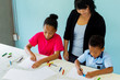 © twinsterphoto - Young teacher giving African American kids an art lesson and teaching how to draw inside indoors room in natural ambient light