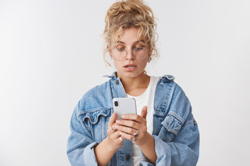 Wall Mural - Portrait worried intense good-looking stylish modern 20s young woman blond curly messy bun wear glasses denim jacket look disturbed nervous smartphone screen reading message, checking grocery list