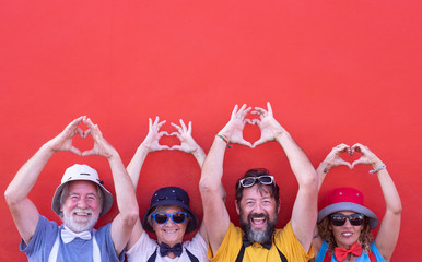 Two couples of people with raised arms form a heart with their hands. Together in friendship and love. Colorful clothing. Red wall on background