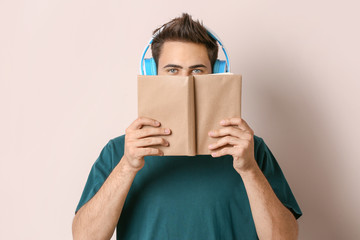 Poster - Young man listening to music and reading book on light background