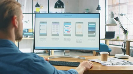 Young Professional Works on a Laptop at His Desk in the Creative Office. Notebook Screen Shows Mobile Phone Application Design, Software UI Development. In the Background Creative Modern Office
