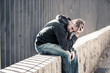 Unhappy depressed caucasian male sitting on urban street feeling
