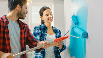 Young Beautiful Couple Decorate Their New Apartment. Husband and Wife are Painting the Wall with Rollers that are Dipped in Light Blue Paint. Renovations at Home.