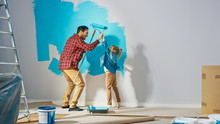 Young Father Is Showing How To Paint Walls To Cute Small Daughter. They Give High Give To Each Other. Rollers Are Covered In Light Blue Paint. Room Renovations At Home.