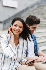 Wall Mural - Happy young amazing loving couple business people colleagues outdoors outside on steps using mobile phone and laptop computer listening music with earphones.