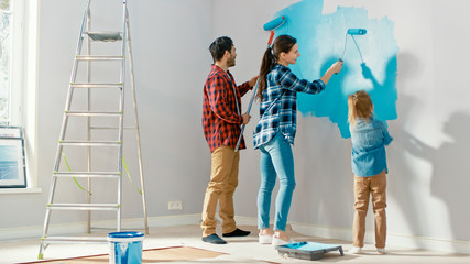 Wall Mural - Family Time Together with Small Daughter. Young Father and Mother Showing Their Child How to Paint a Wall with a Roller. Paint Color is Light Blue. Room at Home is Prepared for Renovations.