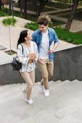 Wall Mural - Amazing loving couple students outdoors outside walking by steps with books.