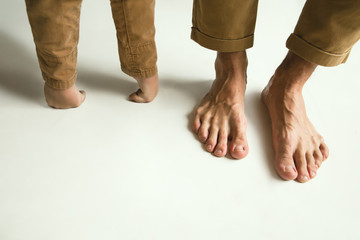 family's legs on white studio background. barefoot dad and son standing together. concept father's d
