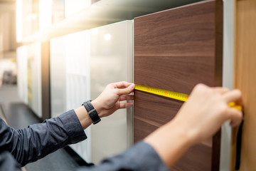 Male hand using tape measure on cabinet panel choosing materials or countertops for built-in furniture design. Shopping furniture and house decoration. Home improvement concept