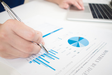 Poster - Close up of the hand holding the pen on the graph of the business worker at the modern white desk. Financial accounting concepts.