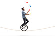 Male juggler with clubs riding a unicycle on a rope